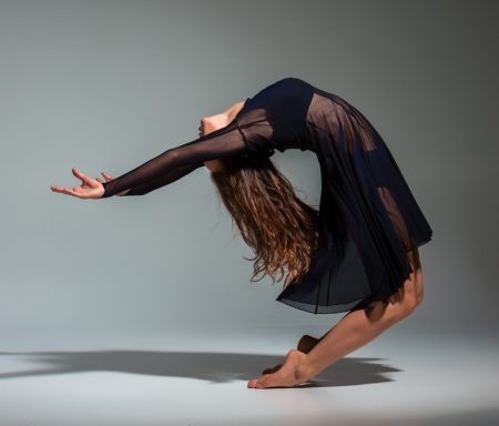 Young beautiful dancer in black dress posing on a dark gray studio background